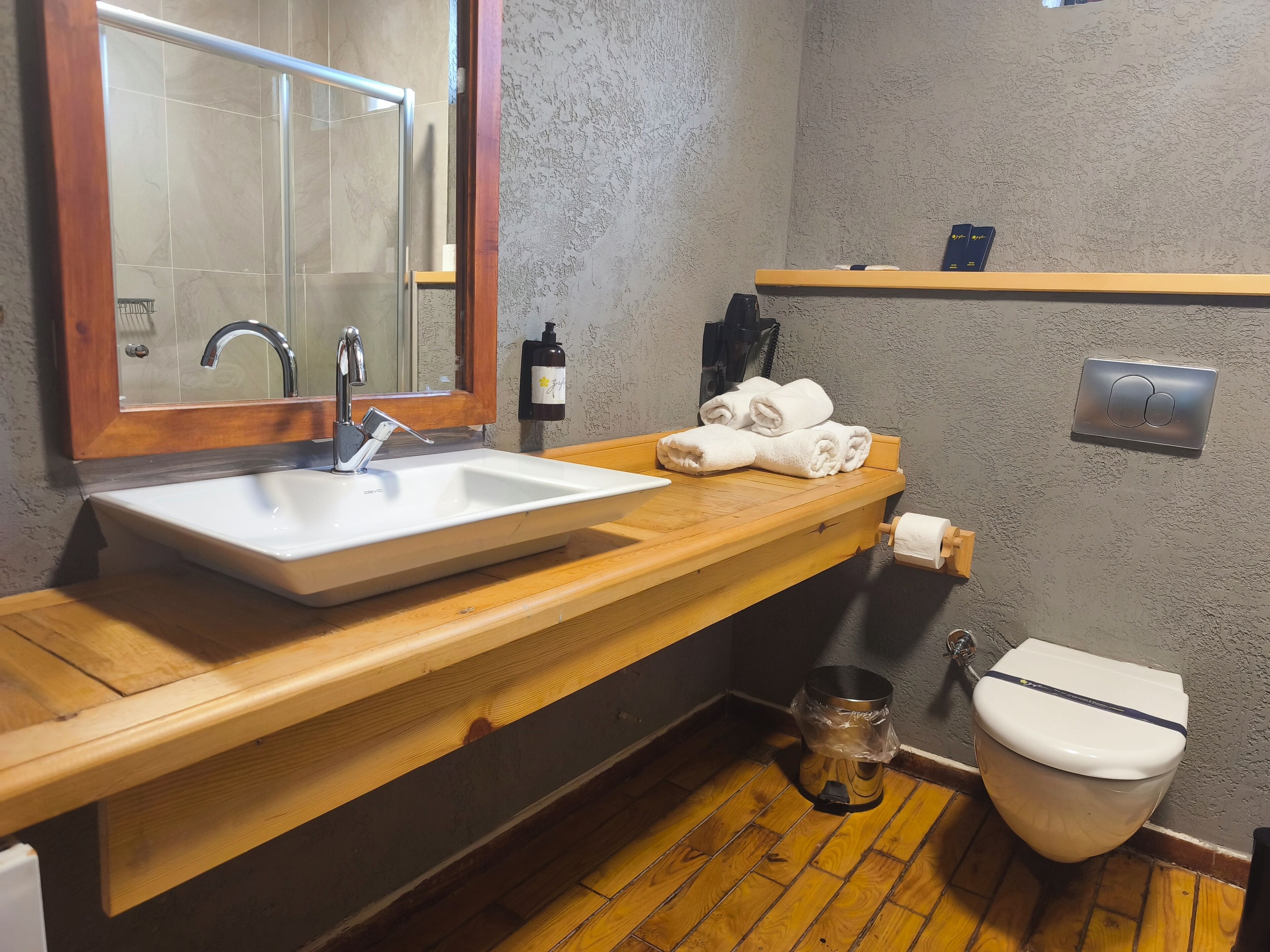 A bathroom with a wooden vanity, a white sink, a mirror, a towel rack, a toilet, and a shower area.