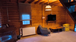 A cozy log cabin interior with a fireplace, a television mounted on the wall, a comfortable chair, and a small table. - Zifin Hotel (Dereli)