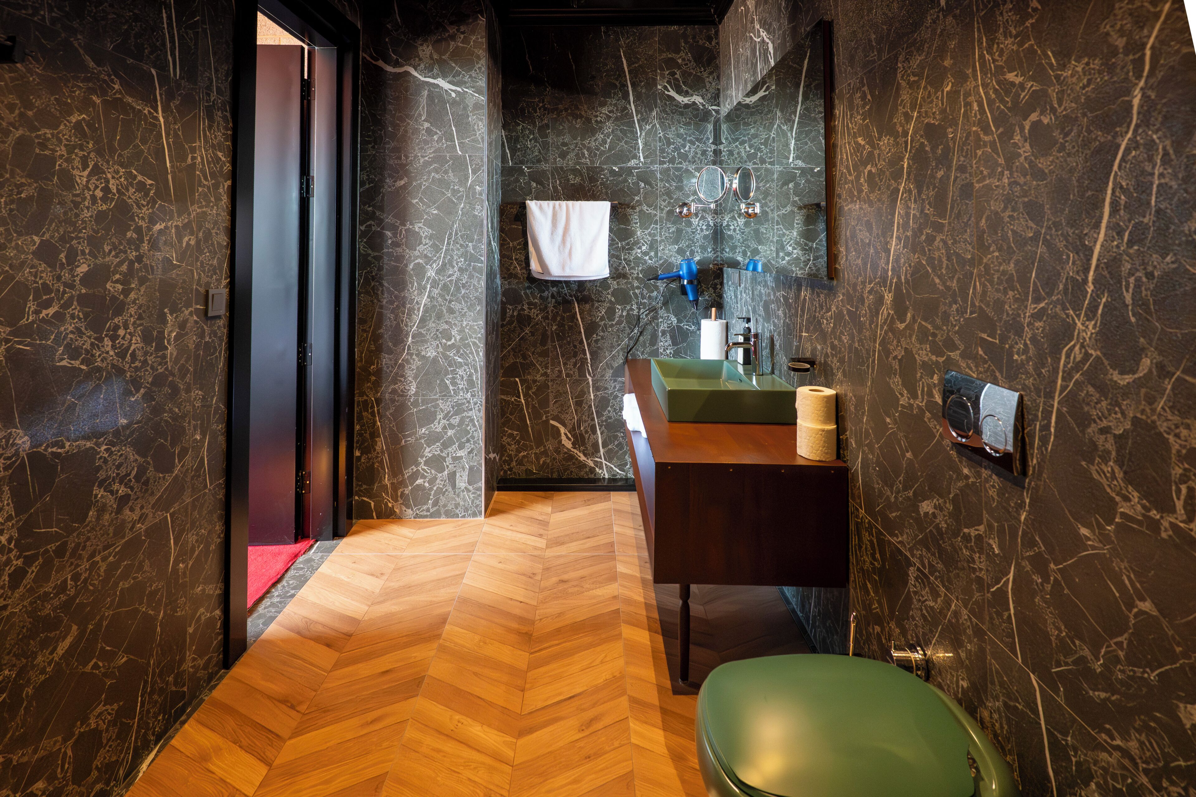 A modern bathroom with a herringbone wooden floor, a green sink, and marble walls.
