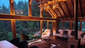A cozy cabin interior with a large window overlooking a forest, a fireplace, and a dining area. - Zifin Hotel (Dereli)