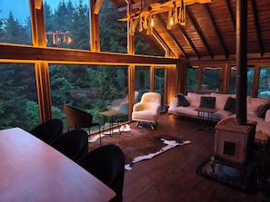 Interior acogedor de una cabaña con un ventanal grande con vista a un bosque, una chimenea y un comedor.