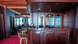A bar area with a curved wooden counter, a red carpet, and a seating area with a chair and a table. - Zifin Hotel (Dereli)