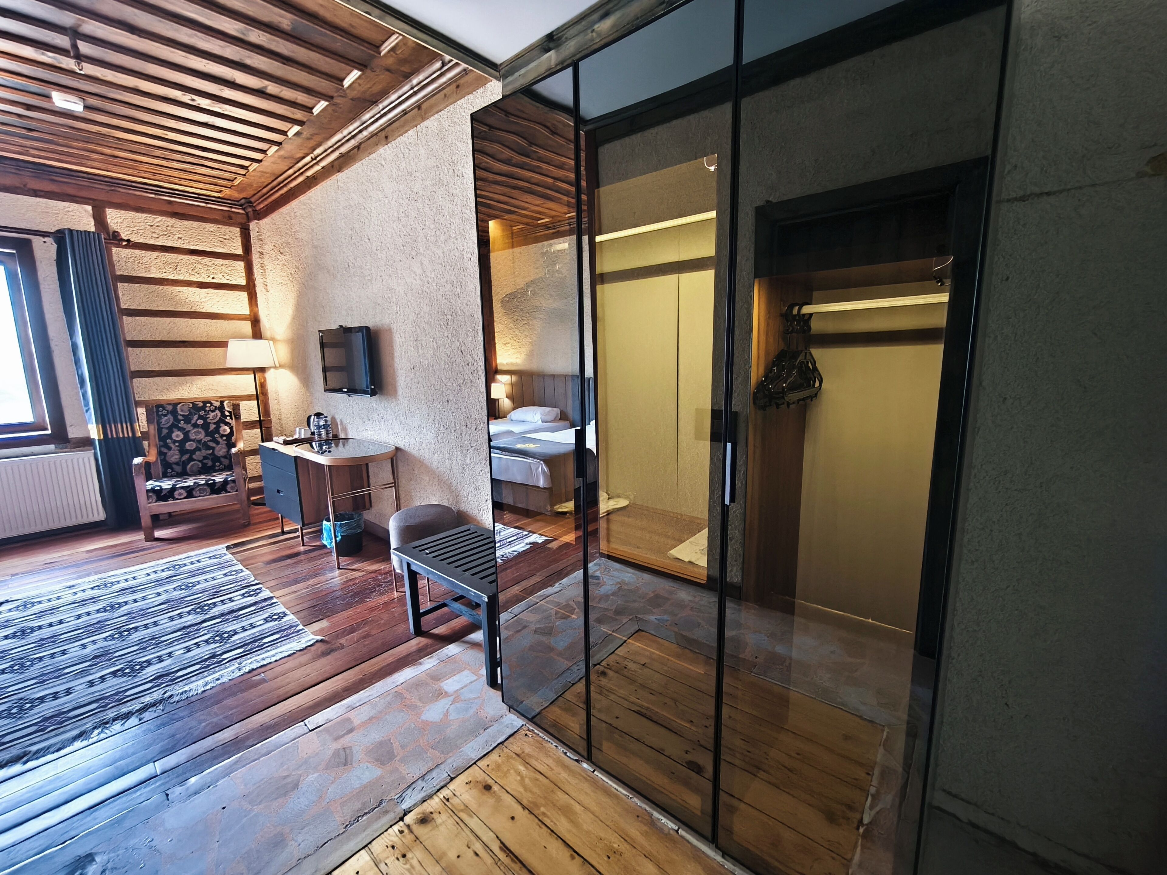 A modern hotel room with a wooden floor, a sofa, a small table, a TV, and a sliding glass door leading to a bathroom.