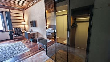 A modern hotel room with a wooden floor, a sofa, a small table, a TV, and a sliding glass door leading to a bathroom.