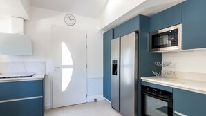 A modern kitchen with a built-in microwave, stainless steel refrigerator, and a white door with a clock. - (107) A la Joie de vivre 2 (Cannes)