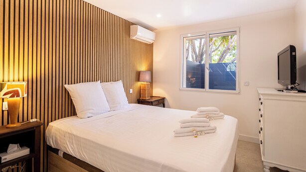 A hotel room with a bed, bedside lamps, a TV, and a window with a view of trees. - (107) A la Joie de vivre 2 (Cannes)