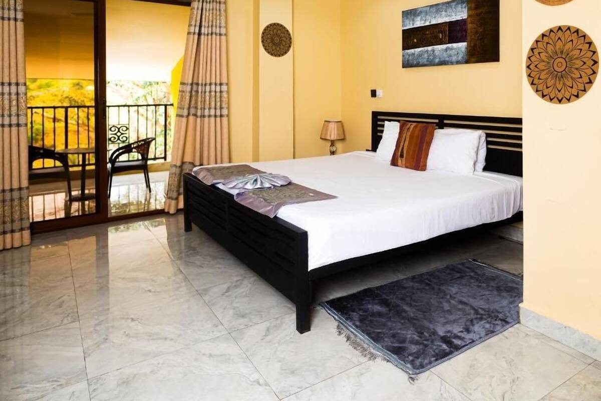 A hotel room with a bed, a balcony with a chair, and a ceiling fan.