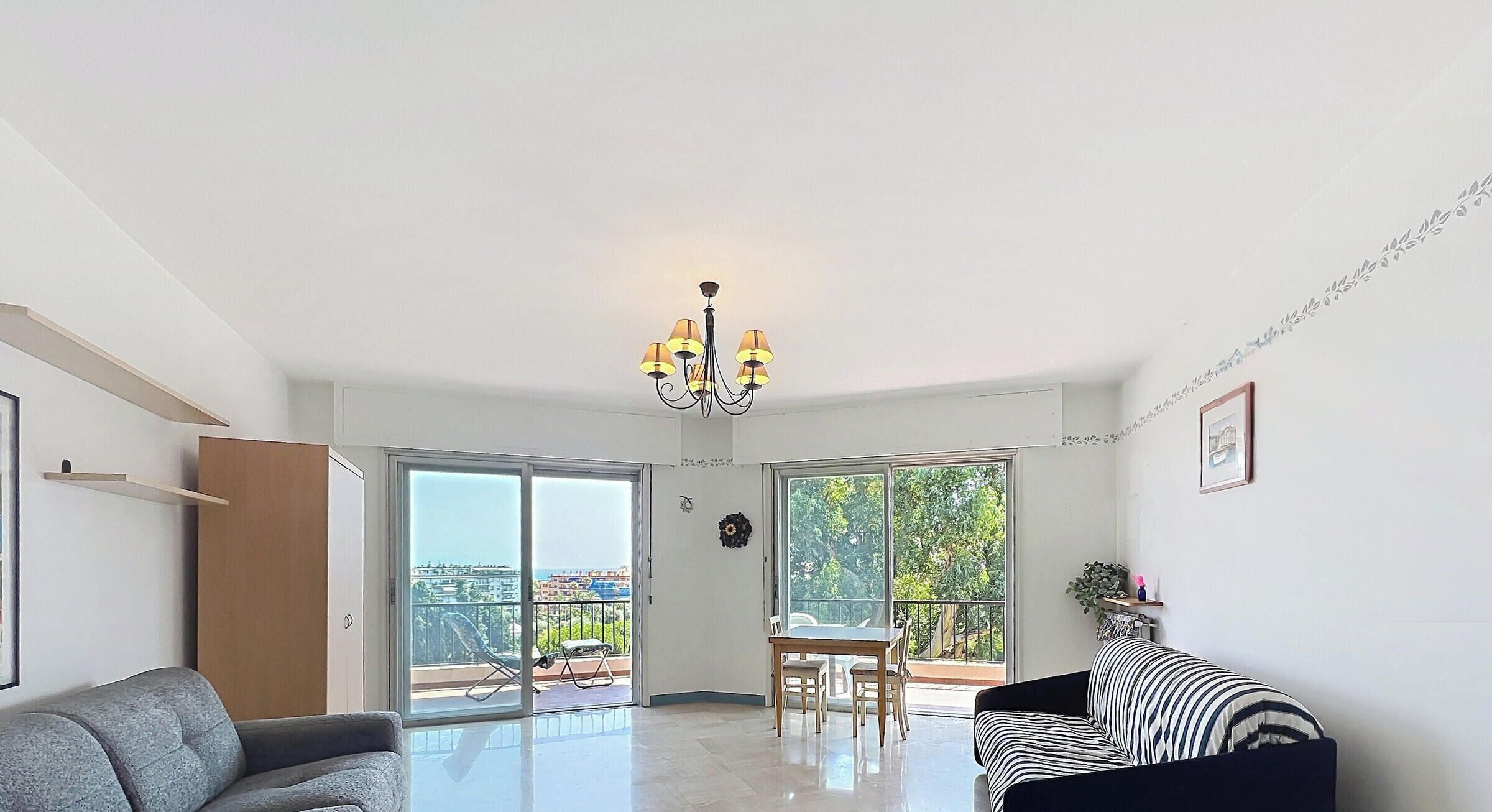 A spacious living room with a sofa, a dining table with chairs, and a chandelier.