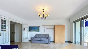 A spacious living room with a grey sofa, a chandelier, a painting, and a wooden wardrobe. - Spacious studio, terrace, sea view - 2 guests (Menton)