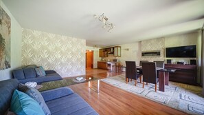 Ein modernes Wohnzimmer mit einer Couch, einem Essbereich mit Stühlen, einer Küche mit Schränken und einem flachbildfernseher an der Wand.