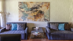 A room with two grey sofas, a small table with a woven basket, and a large abstract painting on the wall. - Apartamenty Sun&Snow VIVA MARIA SPA II (Zakopane)