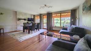 Ein modernes Wohnzimmer mit Essbereich, einer Couch, einem Fernseher und einem Balkon mit Vorhängen.