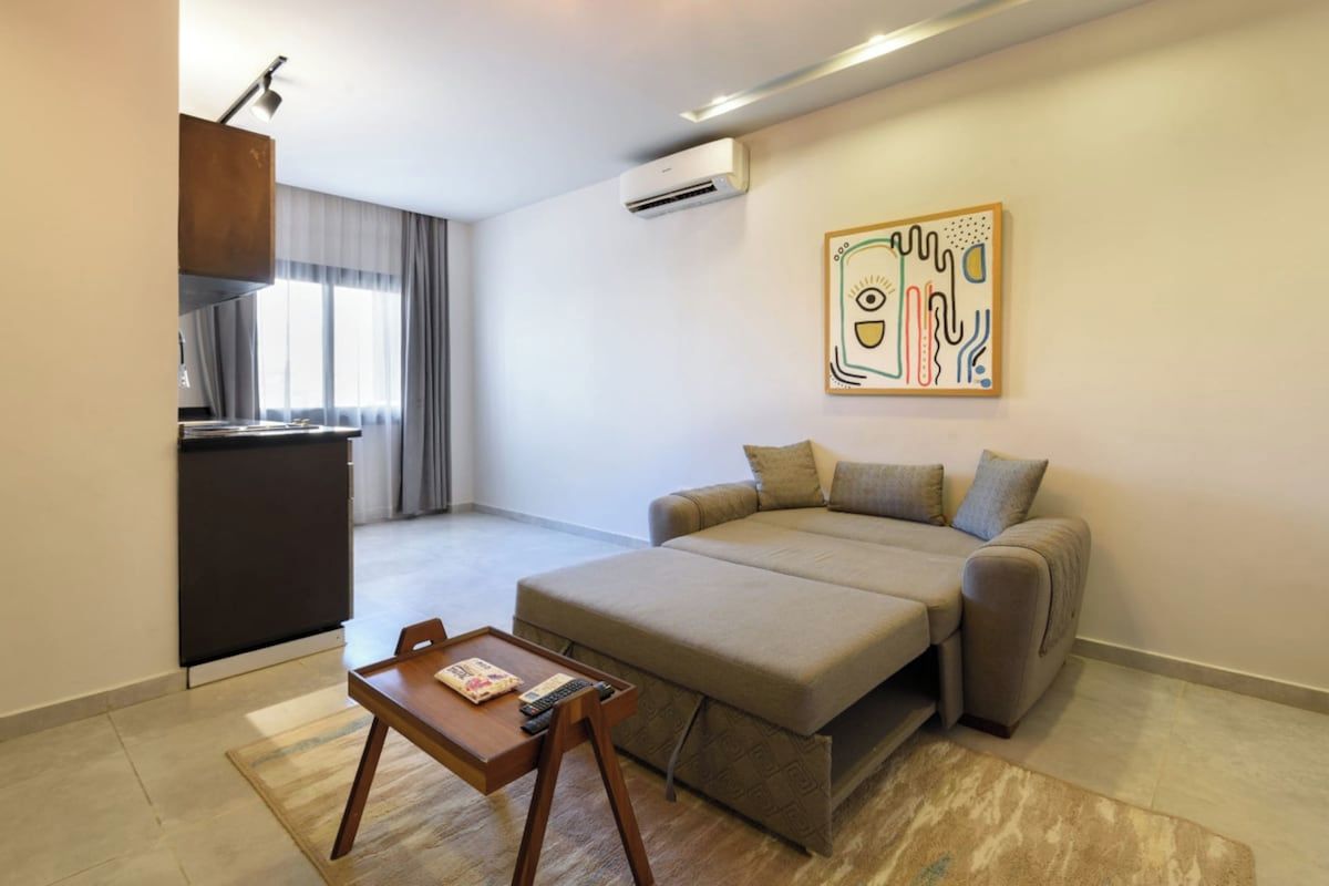 A modern living room with a sofa, a small wooden table, and a kitchen area in the background.