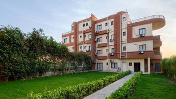 A multi-story residential building with balconies, a paved walkway, and a well-maintained lawn.
