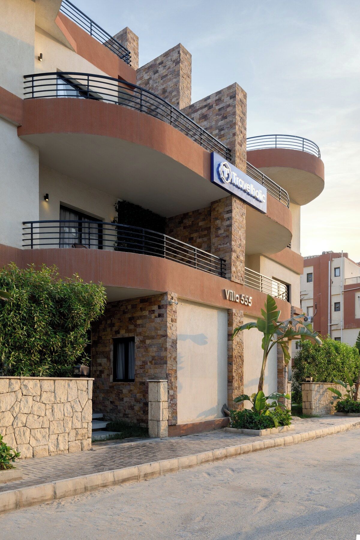 Un edificio de varios pisos con balcones, un letrero que dice 'Travelhotel' y un número de calle visible: Villa 555.