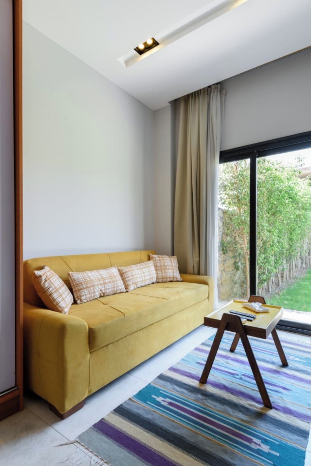 Un salon moderne avec un canapé, une petite table et une vue sur la verdure à l’extérieur.