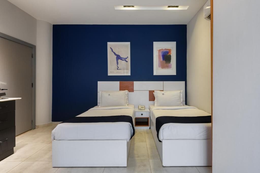A hotel room with two beds, a desk, and artwork on the wall.