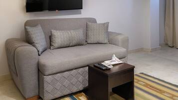 A living room with a sofa, a coffee table, a flat-screen TV mounted on the wall, and a striped rug on the floor.