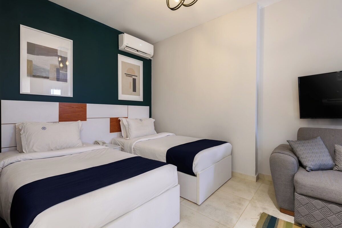 Habitación de hotel con dos camas, un sofá, un televisor de pantalla plana y obras de arte en las paredes.