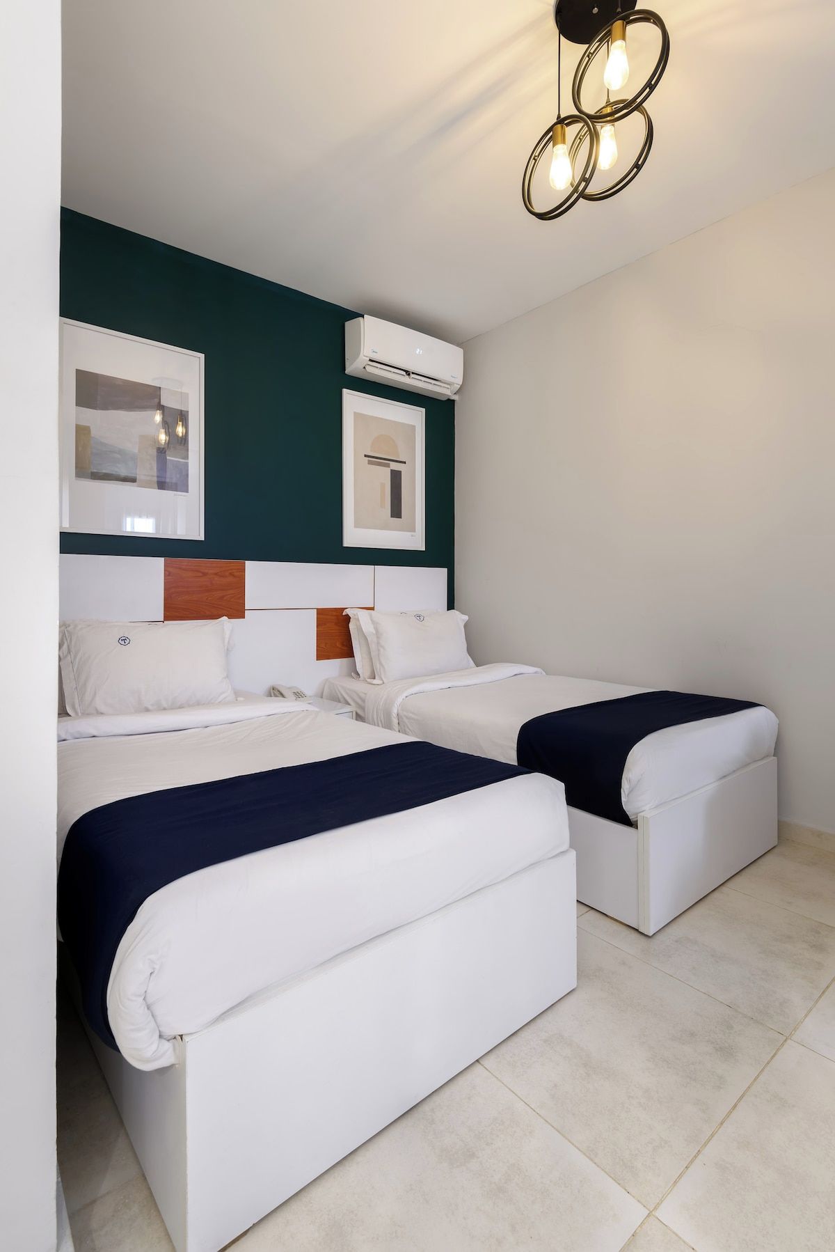 A hotel room with two beds, a ceiling light fixture, and an air conditioning unit.