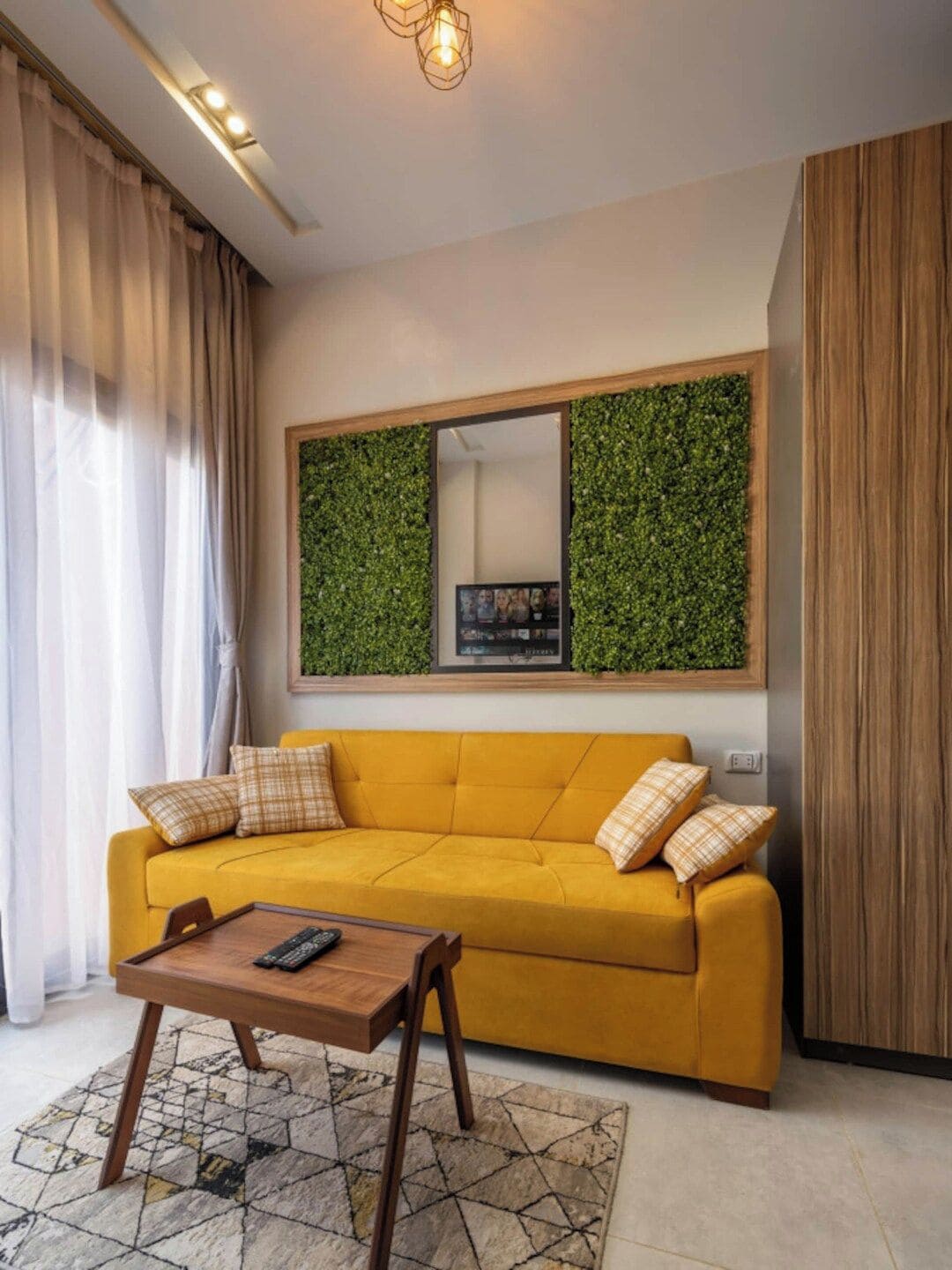 A modern living room with a yellow sofa, a coffee table, and a large mirror with a green wall.
