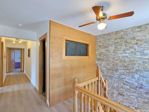 Eine Holztreppe mit Deckenventilator, einer Steinwand und einer Tür zu einem anderen Raum.