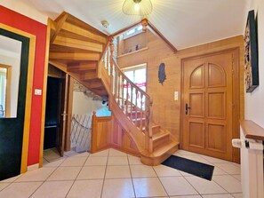 Eine Holztreppe führt zu einer oberen Etage, eine Tür mit Blattmuster und ein Fliesenboden.