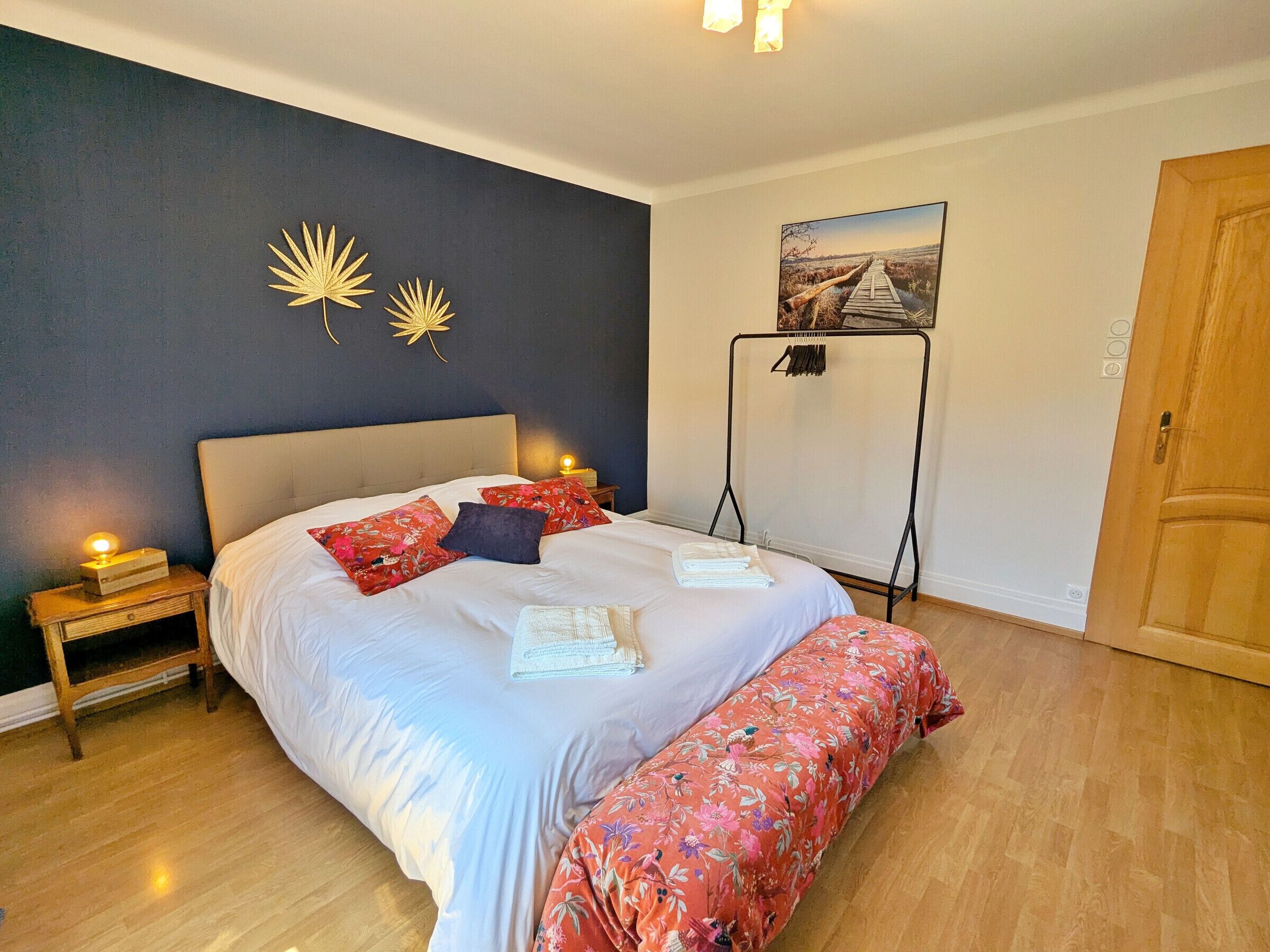 Une chambre à coucher comprenant un lit, des tables de chevet, un banc, une étagère fixée au mur et une porte.
