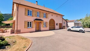 Un bâtiment à deux étages, doté d’un toit en tuiles, d’une entrée centrale avec une grande porte en arc de cercle et d’une allée pavée.
