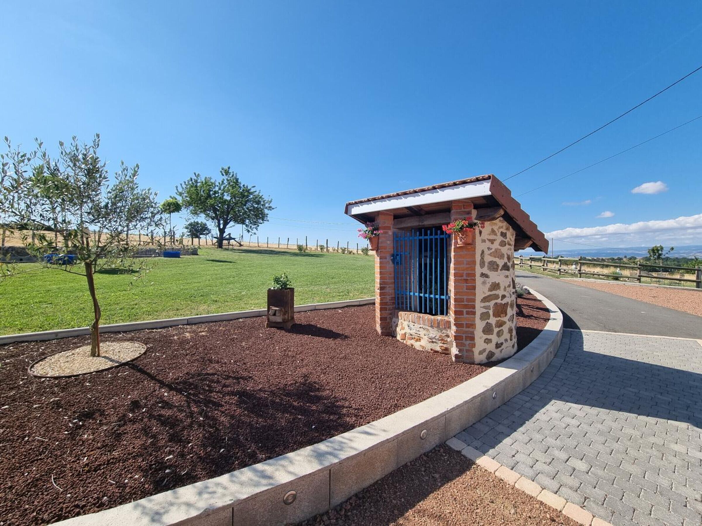 A small stone building with a blue door, surrounded by a landscaped area with mulch and a paved walkway.