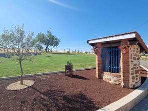 Um pequeno edifício de tijolos com um portão azul, rodeado por um jardim ajardinado com uma árvore e um vaso.