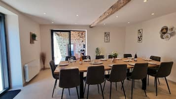 Comedor con una mesa larga dispuesta para seis personas, rodeada de sillas, con una pared de piedra y techo de vigas de madera.