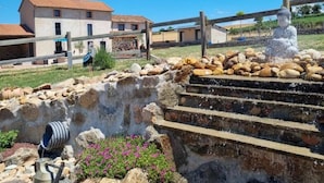 Una estructura de piedra con fuente de agua, rodeada por una cerca de madera, y un edificio al fondo.