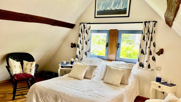 A bedroom with a large bed, a chair, a desk, and a window with curtains.