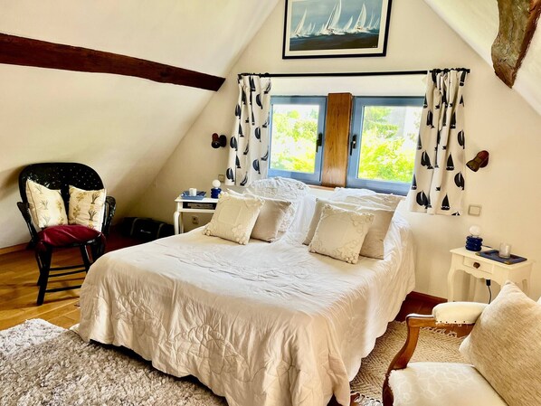 A bedroom with a large bed, a chair, a desk, and a window with curtains.