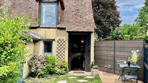 A house with a sloped roof, a visible chimney, a small garden with stepping stones, and a wooden deck with outdoor furniture.