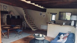 A living room with a sofa, a coffee table, a dining table with chairs, a staircase, and a kitchen area.