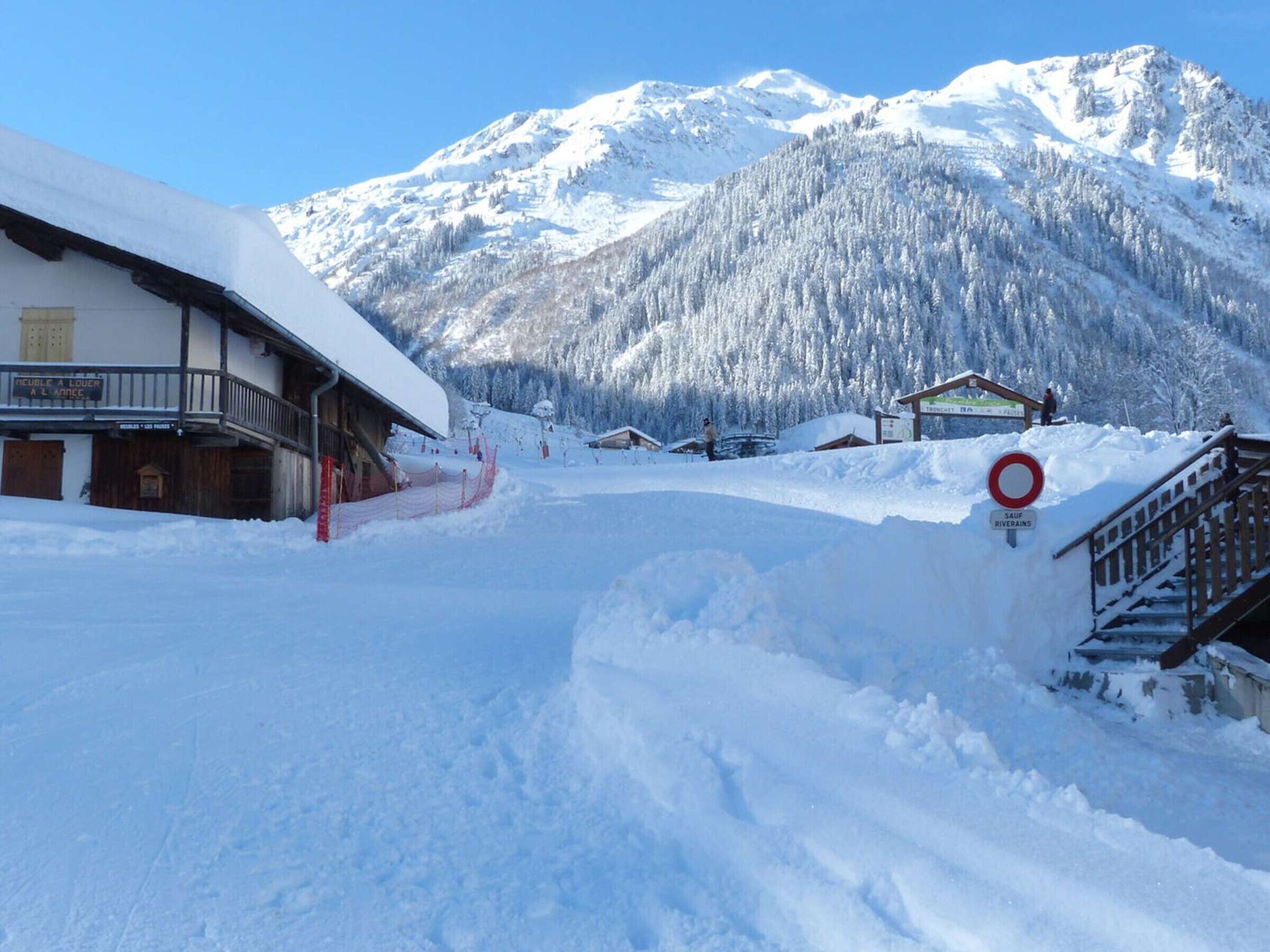 A snow-covered mountain path leading to a building with a sign indicating a ski lift.