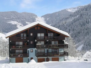 Ein mehrstöckiges Holzchalet mit Balkonen vor einer verschneiten Berglandschaft.