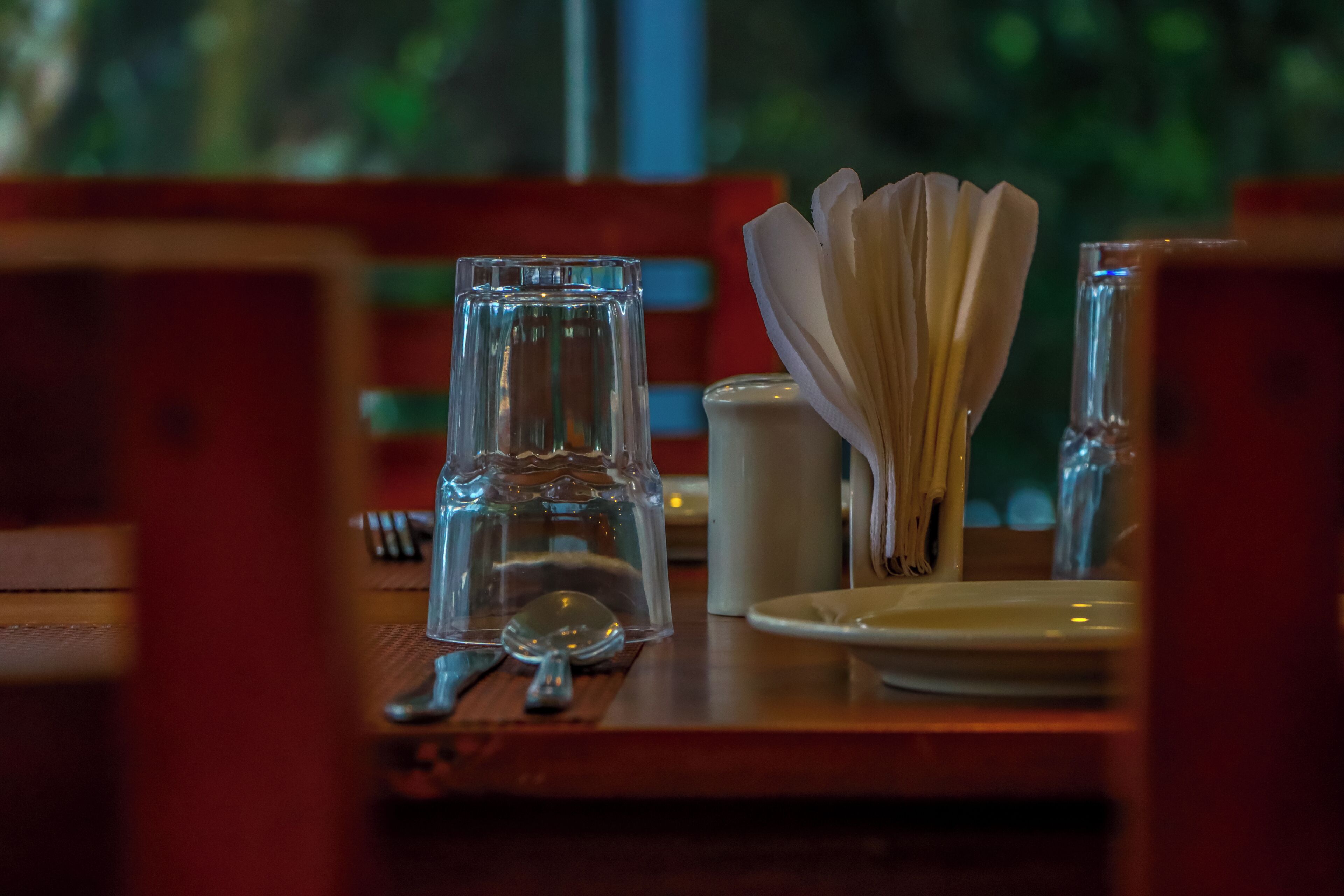 Een eettafel gedekt met een glas, een zoutvaatje, een servetdispenser en een lepel.