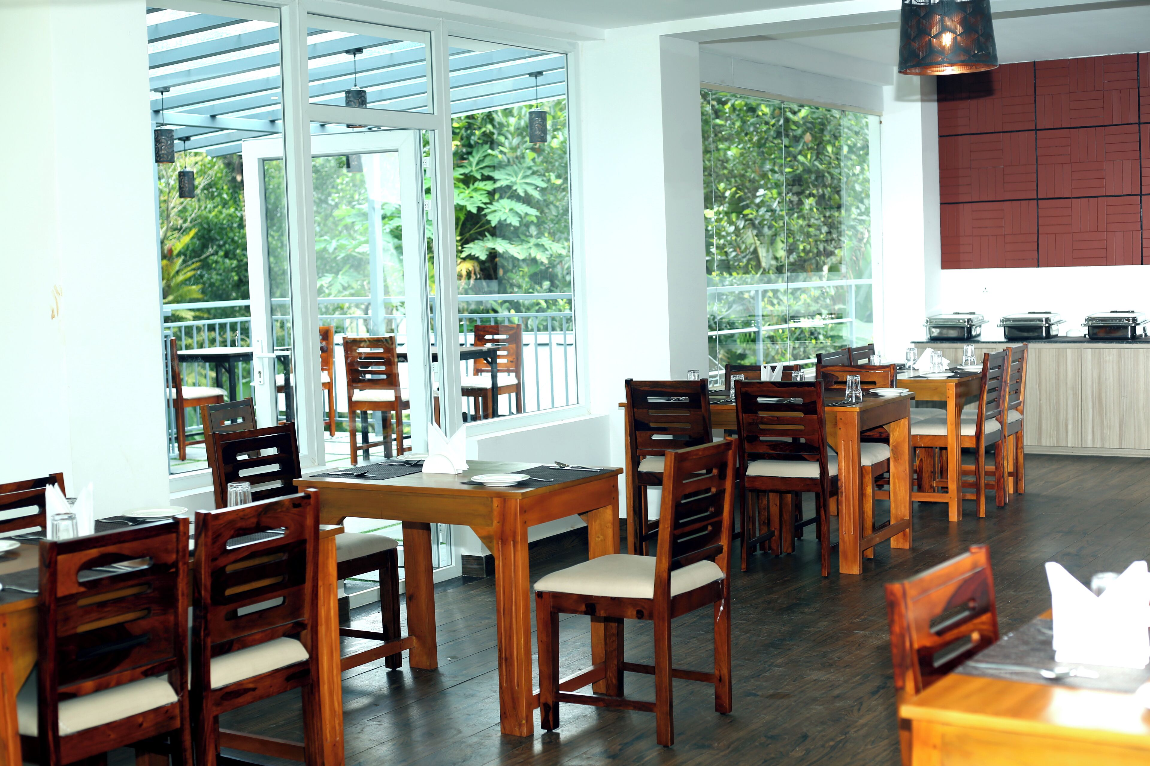 A restaurant with wooden tables and chairs, large windows, and a kitchen area.