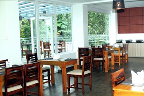 A restaurant with wooden tables and chairs, large windows, and a kitchen area. - Winter Note Resort (Devikolam)
