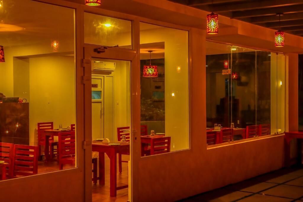 A restaurant with multiple tables and chairs, large windows, and hanging lanterns.