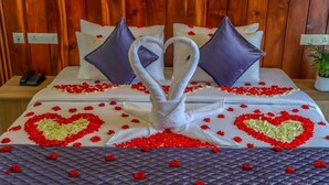 Un lit décoré de serviettes et d’oreillers disposés en forme de cœur, entouré de pétales de roses rouges.