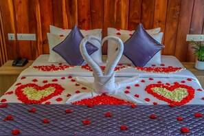 Un lit décoré de serviettes et d’oreillers disposés en forme de cœur, entouré de pétales de roses rouges.