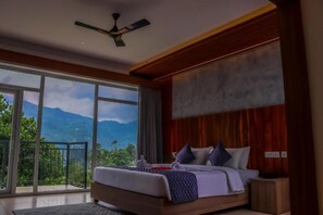 Un dormitorio con una cama grande, un ventilador de techo y vistas a las montañas a través de amplios ventanales.