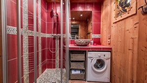 Een kleine badkamer met een douche, een wasmachine en een wastafel met een decoratieve kom.
