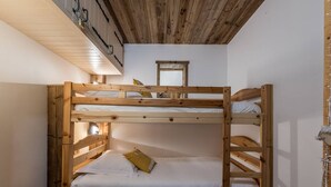 Een slaapkamer met een stapelbed, houten plafond en een klein nachtkastje.
