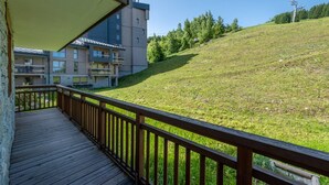 Een houten terras met uitzicht op een groene heuvel en een meer verdiepingen tellend gebouw op de achtergrond.