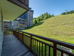 Eine Holzterrasse mit Blick auf einen grasbewachsenen Hügel und ein mehrstöckiges Gebäude im Hintergrund.